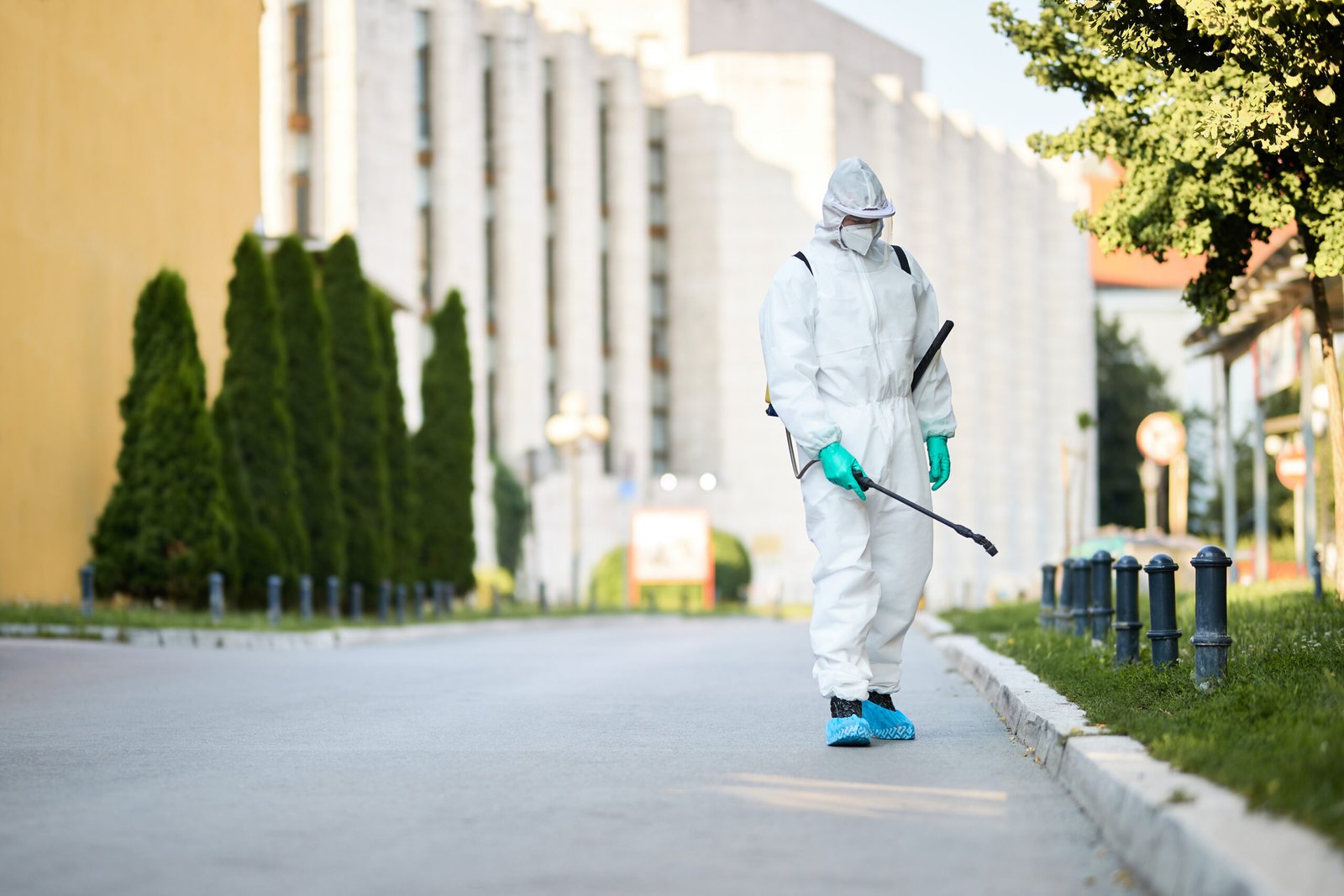 Disinfectant worker in protective suit sanitizing empty city streets during COVID-19 epidemic.